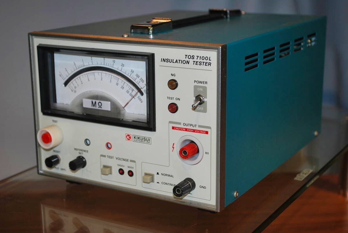 Angled view of a KIKUSUI TOS 7100L insulation tester showing the analog MΩ meter, front panel controls, and side casing.