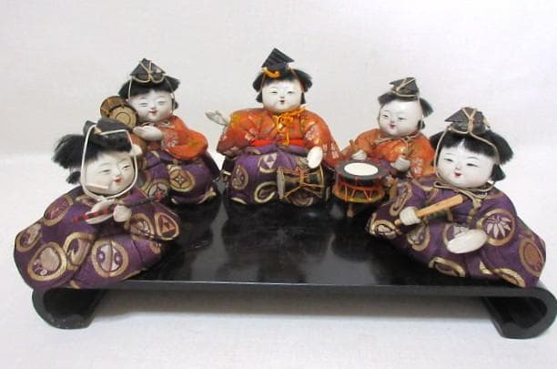 Five small traditional Japanese kimekomi musician dolls in purple and orange robes seated on a black lacquer stand.