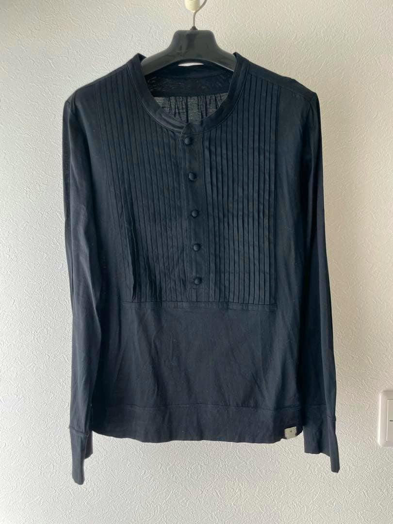 Front view of the long-sleeve cotton T-shirt showing pleated decoration and a row of fabric-covered buttons hanging on a hanger.