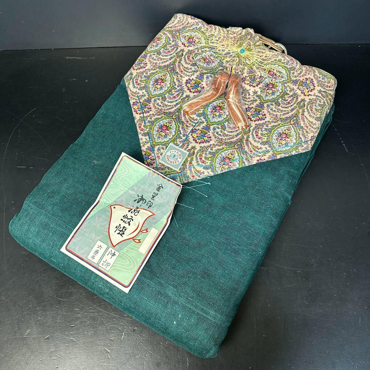 Folded dark green hemp mosquito net with a patterned decorative panel and attached paper tag on a black surface.