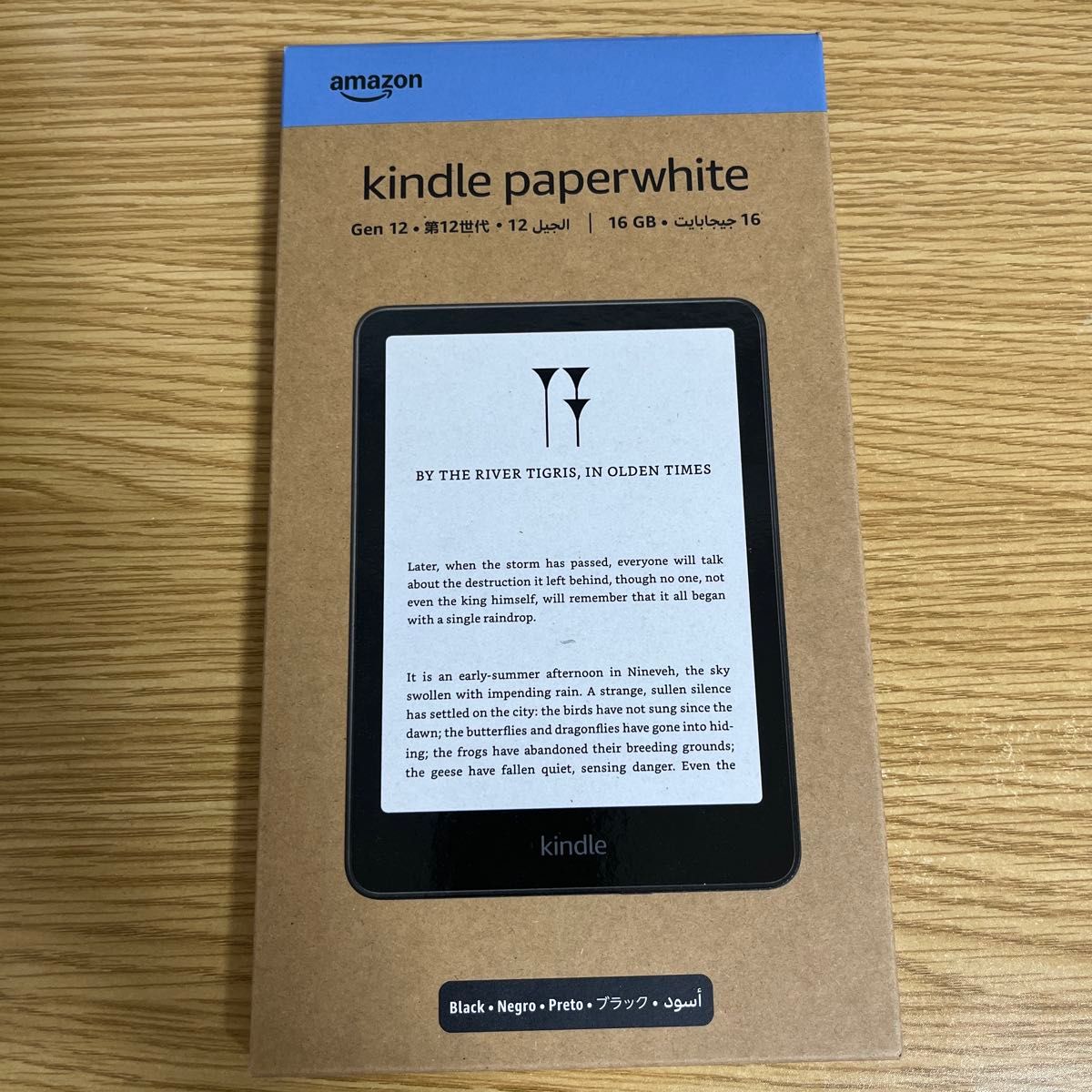 Front of a boxed Kindle Paperwhite 7-inch 16GB (Black) retail packaging placed on a wooden surface.
