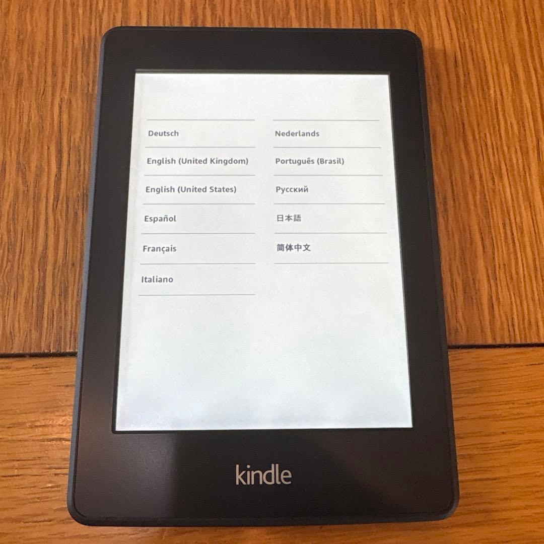 Front view of a Kindle Paperwhite showing the language selection screen on a wooden surface.