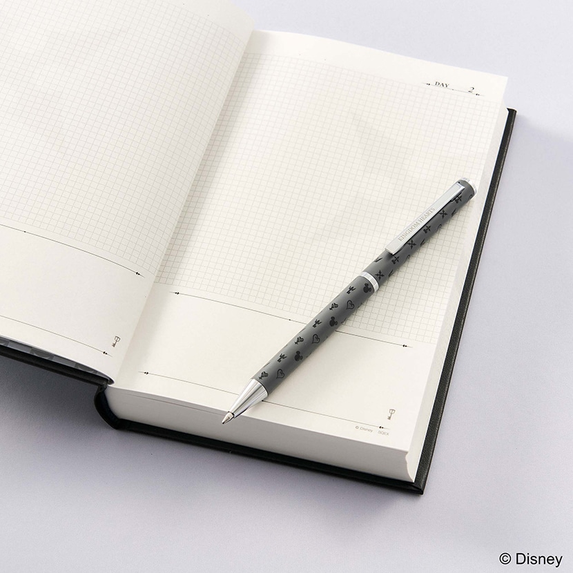 A Kingdom Hearts black ballpoint pen with small motif patterns resting on an open notebook.