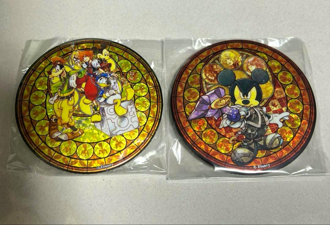 Two round Kingdom Hearts can badges with stained-glass style artwork are shown in clear plastic sleeves on a light surface.