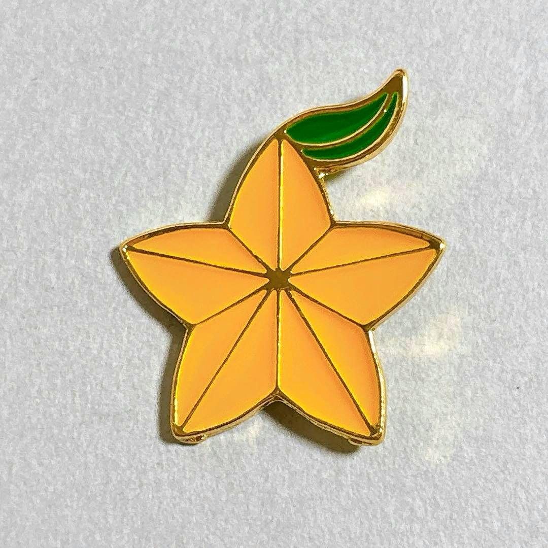 Orange star-shaped Paopu fruit enamel pin with gold outline and a small green leaf on a light background.