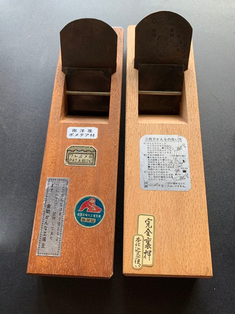 Two wooden hand planes with metal blades and labels, photographed from above on a dark surface.