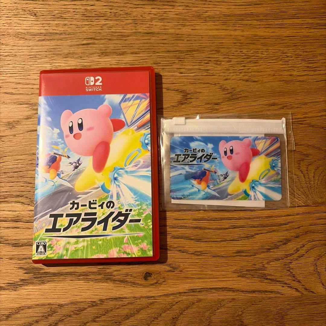 Closed Nintendo Switch game case for "カービィのエアライダー" with Kirby cover art shown next to a small sealed card on a wooden surface.