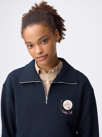 A woman wearing a navy half-zip pullover jacket with Kirby embroidery on the chest.