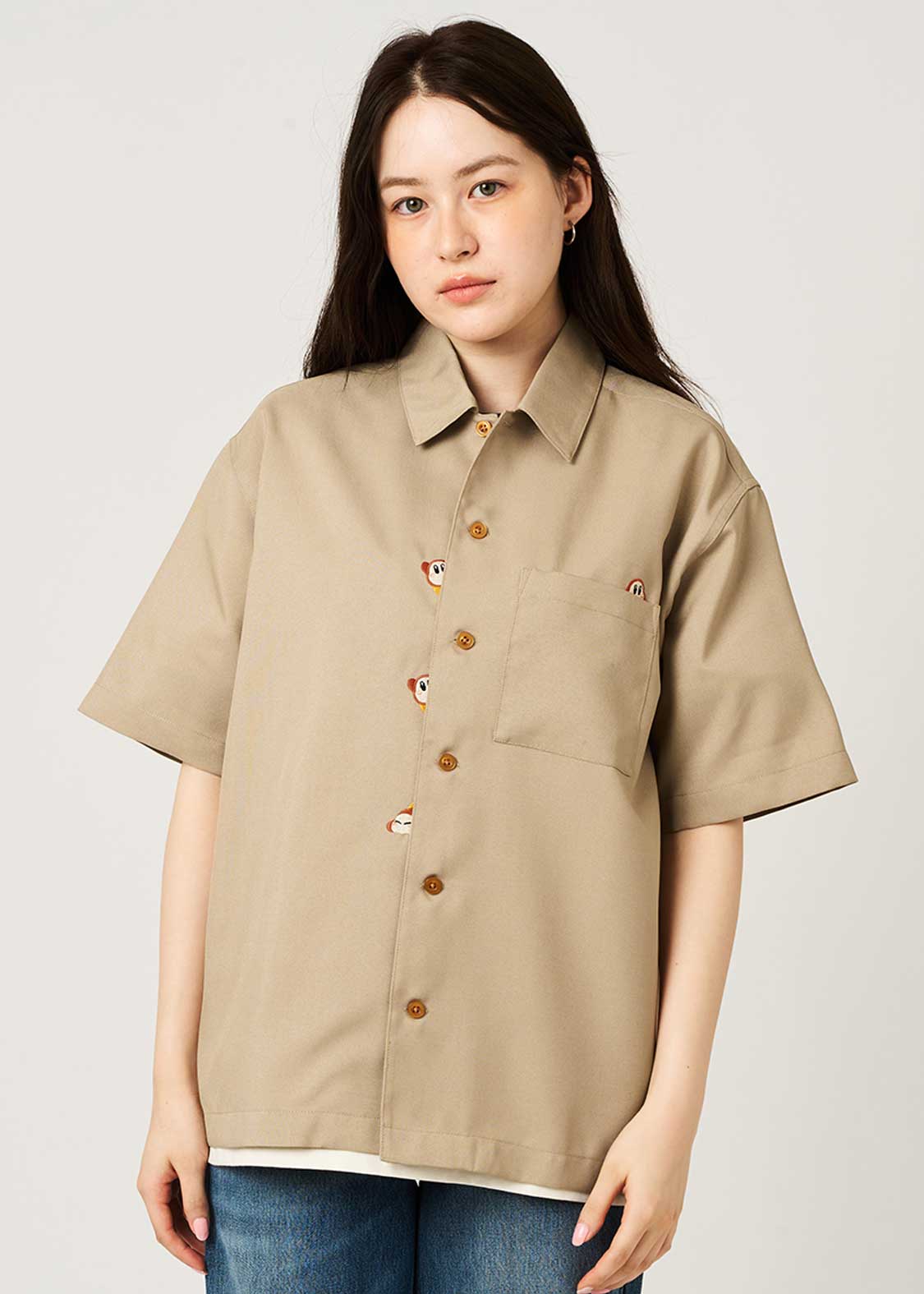 Woman model wearing a beige oversized short-sleeve button-up shirt shown from the front.