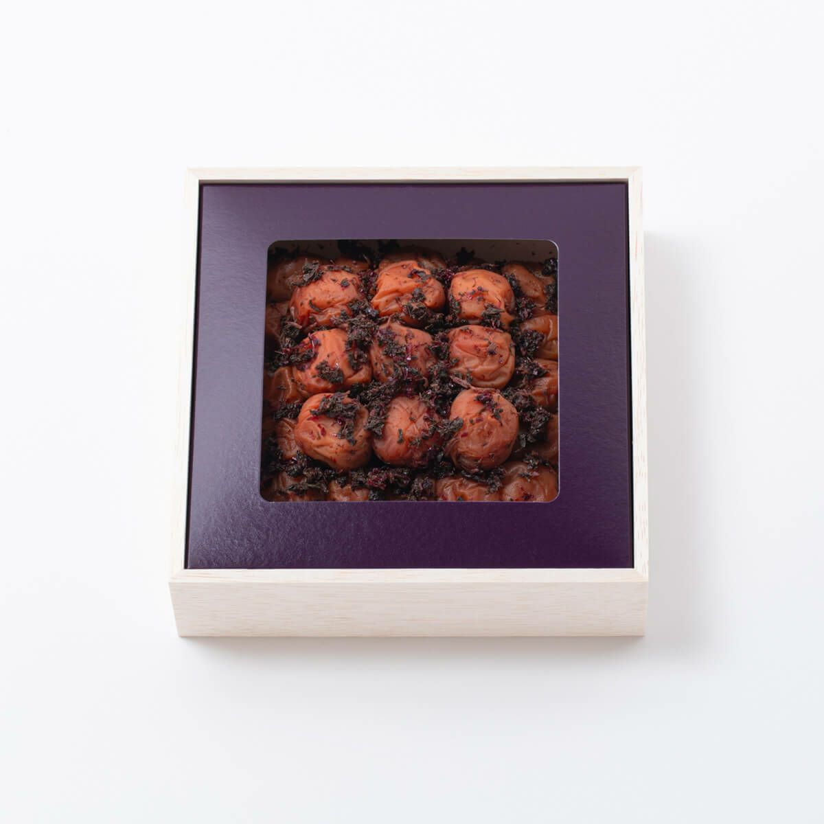 Top view of a square wooden box of preserved plums showing the plums through a purple-framed window.