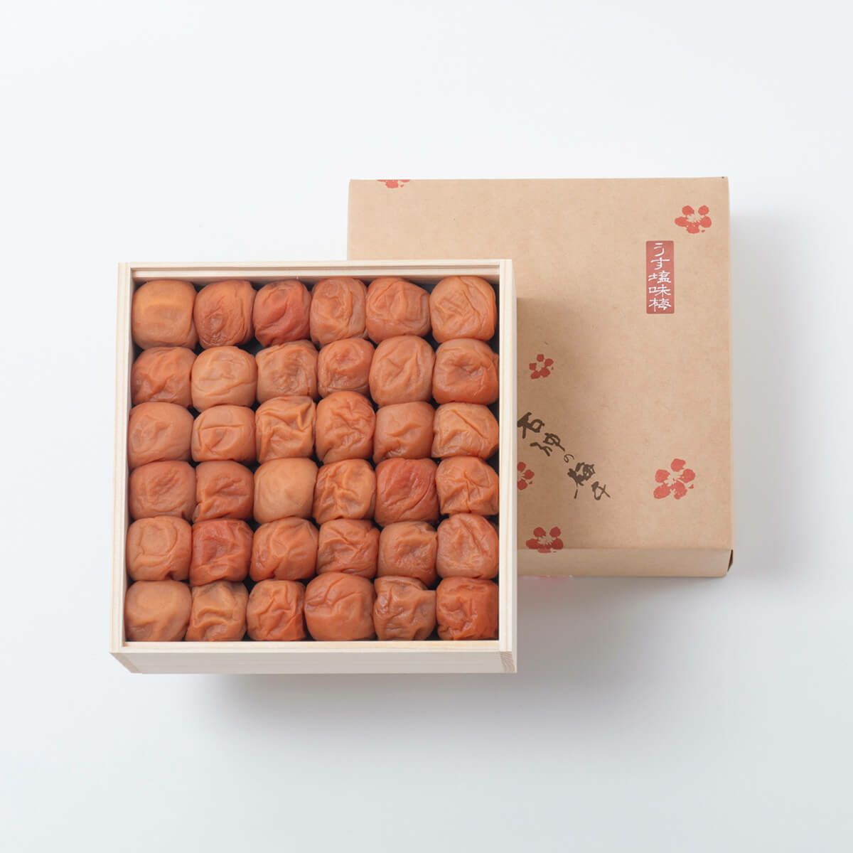Wooden box of preserved plums neatly arranged in rows with the decorative cardboard lid placed beside it.