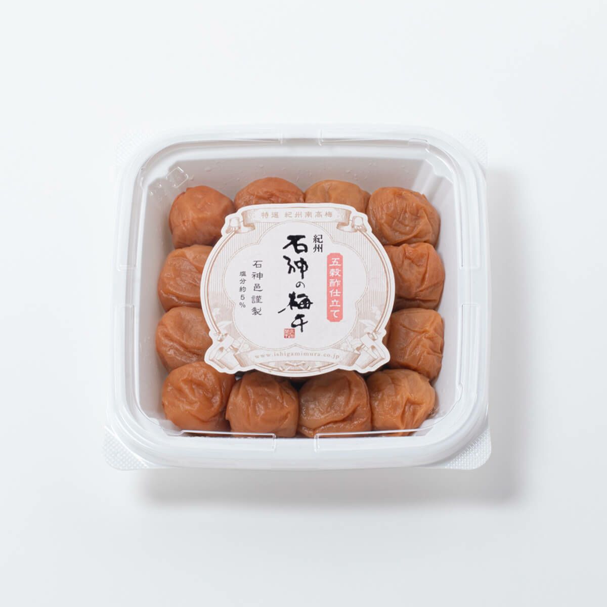 Top-down photo of a square PET container of preserved plums with a round label on the lid.