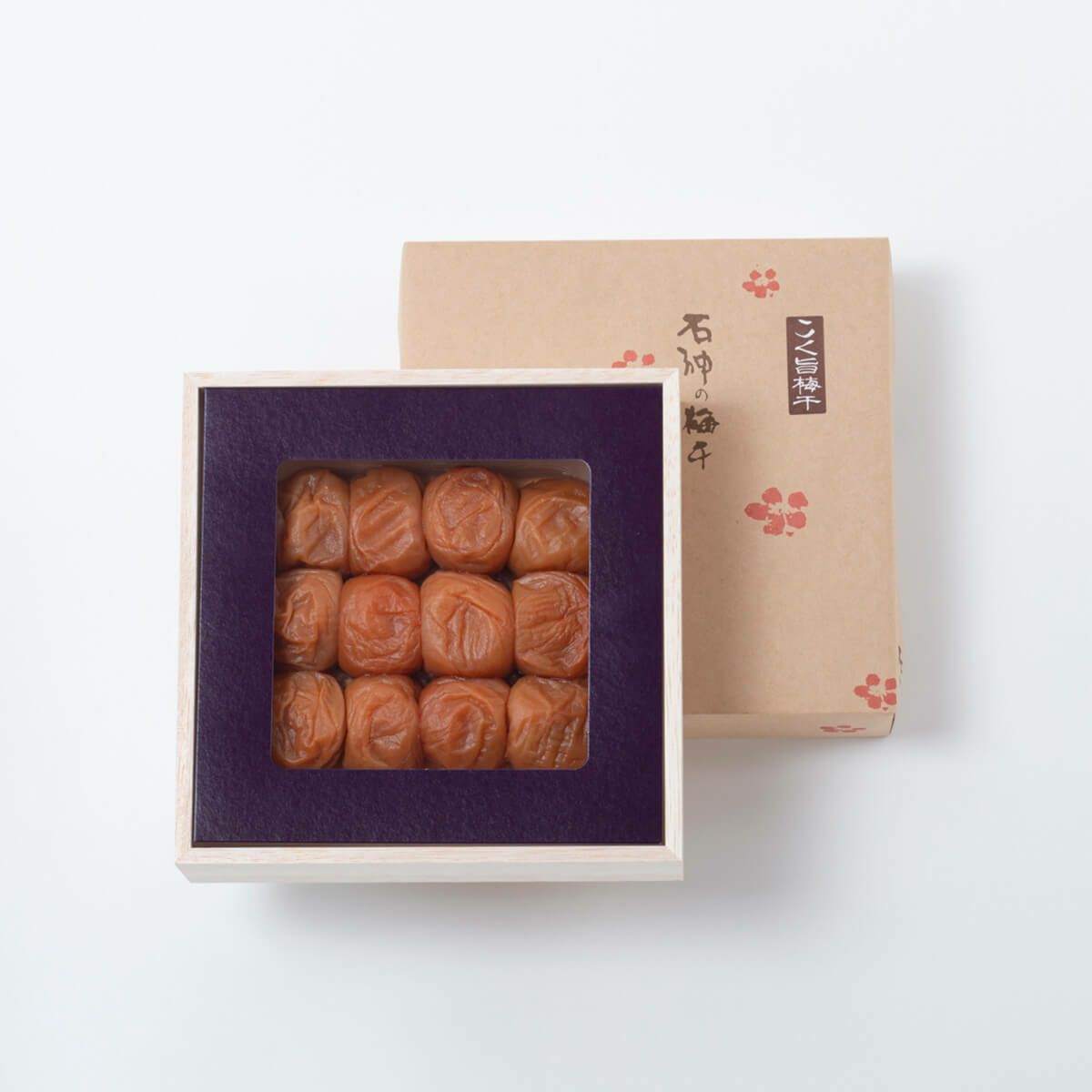 A wooden box of preserved plums (umeboshi) in a square tray with the decorative lid placed behind it.
