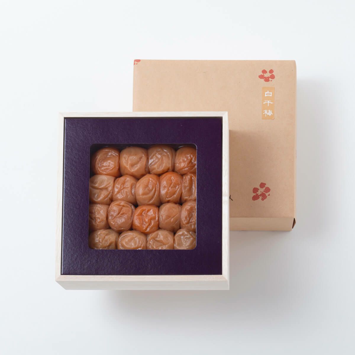 Wooden box of preserved plums shown with its cardboard outer box behind on a white background.