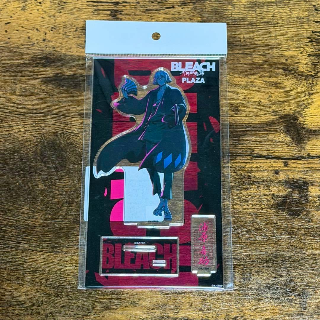 Packaged PLAZA acrylic stand of 浦原喜助 (Bleach) showing the character acrylic figure and base inside a clear plastic sleeve on a wooden surface.