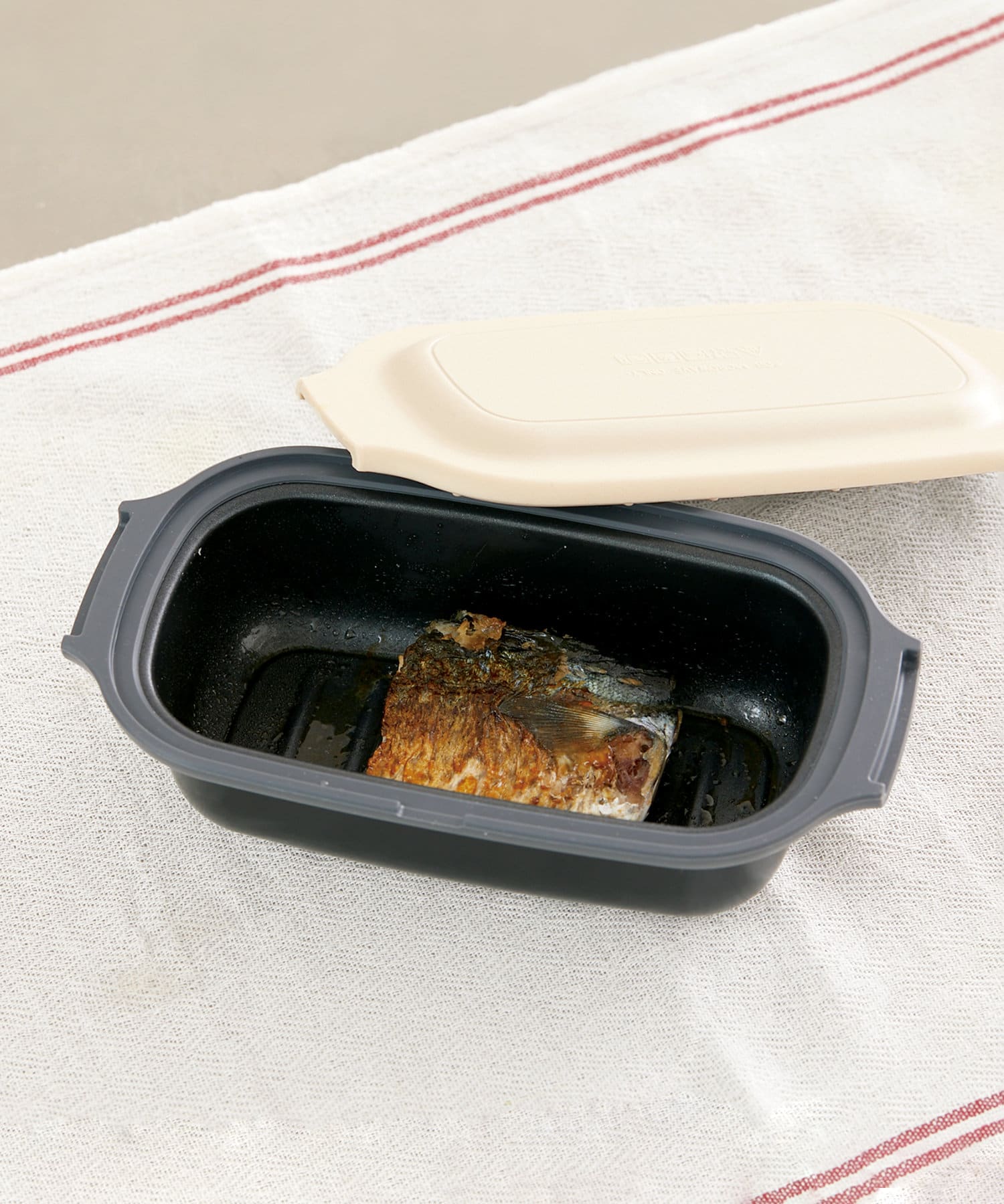 Rectangular microwave cooking tray with the lid partially removed showing cooked fish inside.