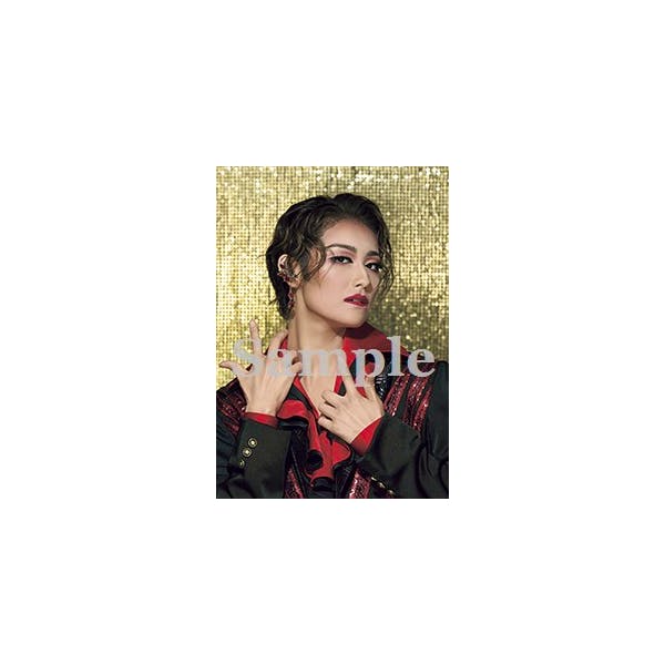 Portrait-style photograph of a stage performer in makeup and costume against a gold background with a 'sample' watermark.