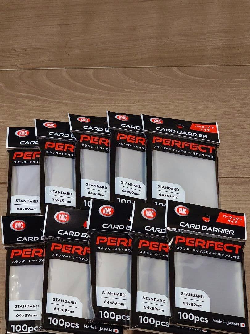 Photo showing multiple KMC "Perfect" standard 64×89mm 100pcs card inner sleeve packages arranged on a wooden surface.