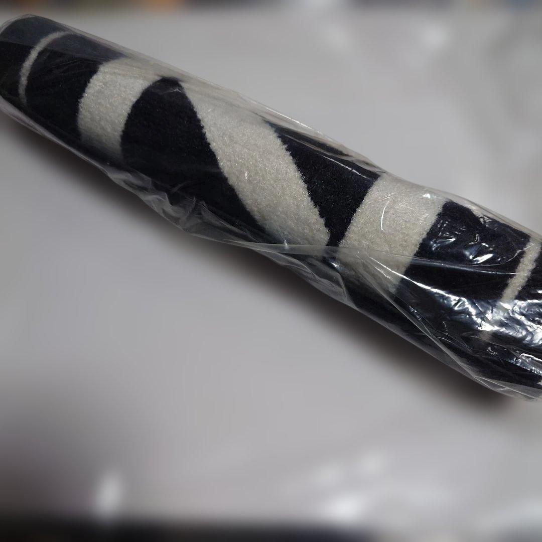 Rolled KMNZ floor mat/rug wrapped in clear plastic showing a black and white striped pattern.