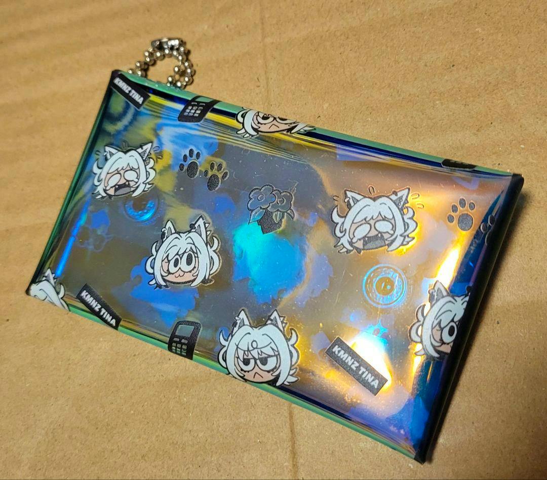 Holographic clear plastic pass case decorated with repeating KMNZ Tina character faces, paw prints, and a small ball chain.