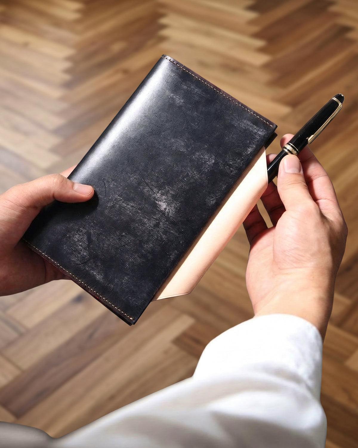 Hands holding a KNOX Lucent Bible 13mm system notebook cover with a pen inserted in the cover pocket.