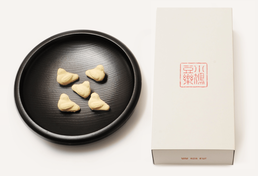 A white rectangular product box next to a black plate holding five small bird-shaped sugar candies.