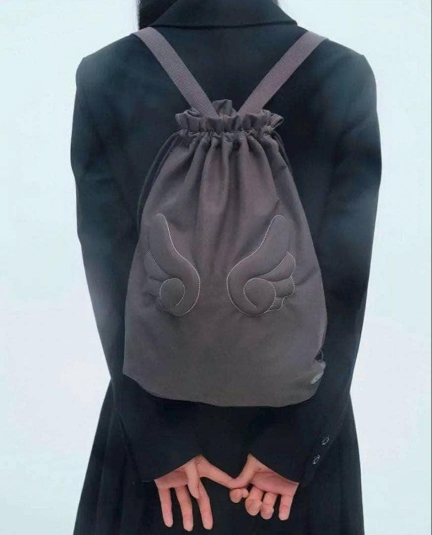 A gray drawstring backpack with stitched wing-shaped details shown worn on a person's back.