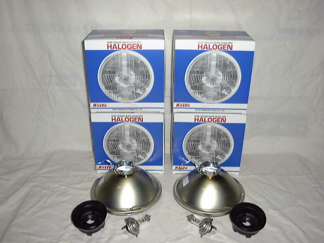 Two round car headlamp assemblies with bulbs and four halogen headlamp boxes on a cloth background.