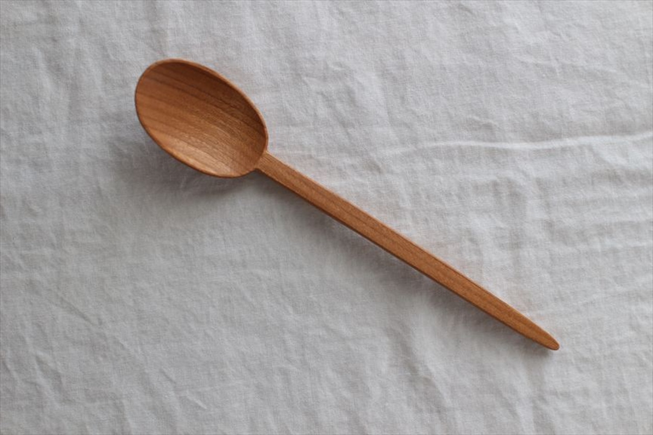 A single wooden spoon with a long handle lying on a light cloth background.