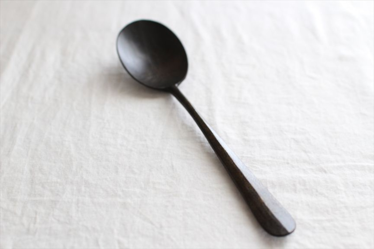 A wooden soup spoon laid diagonally on a light cloth background.
