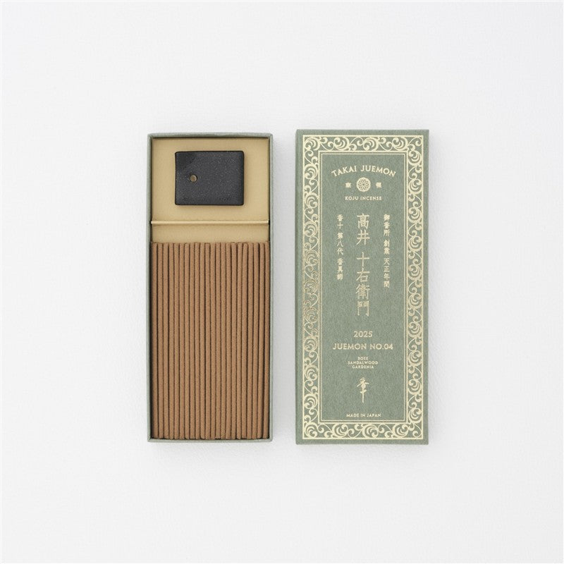 Top-down photo of an open incense box showing aligned incense sticks and a small ceramic holder beside the decorative lid.
