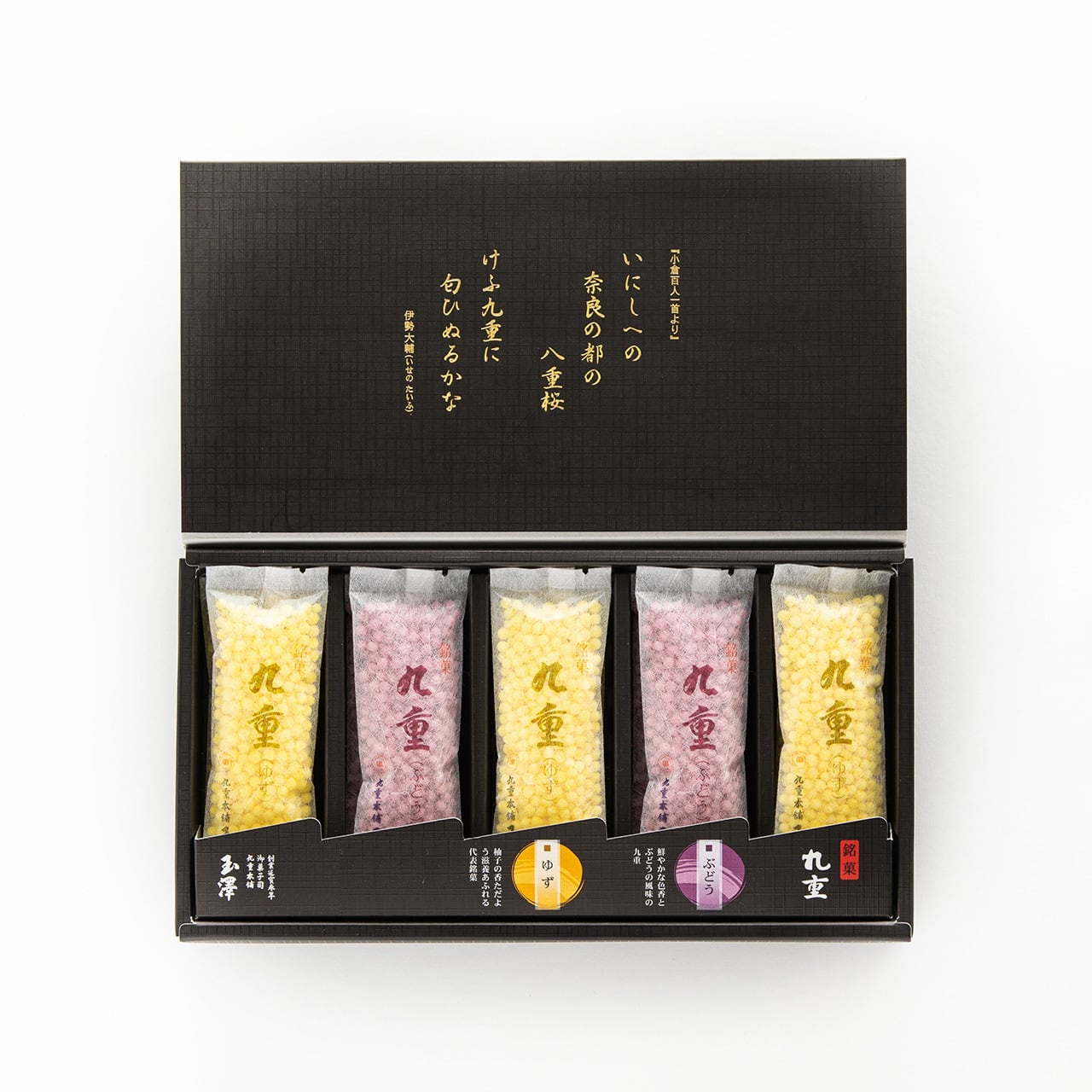 Opened black gift box showing individually wrapped yellow and pink packets of flavored sugar candy for drinks arranged in a tray.