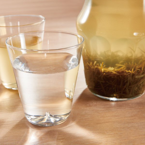 A glass of clear kelp-infused water next to a jar containing soaked dried seaweed on a wooden surface.