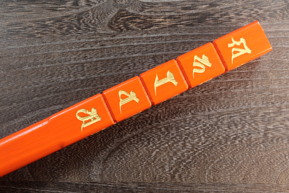 Close-up of an orange lacquered kongōzue walking stick showing gold characters on a wood surface.