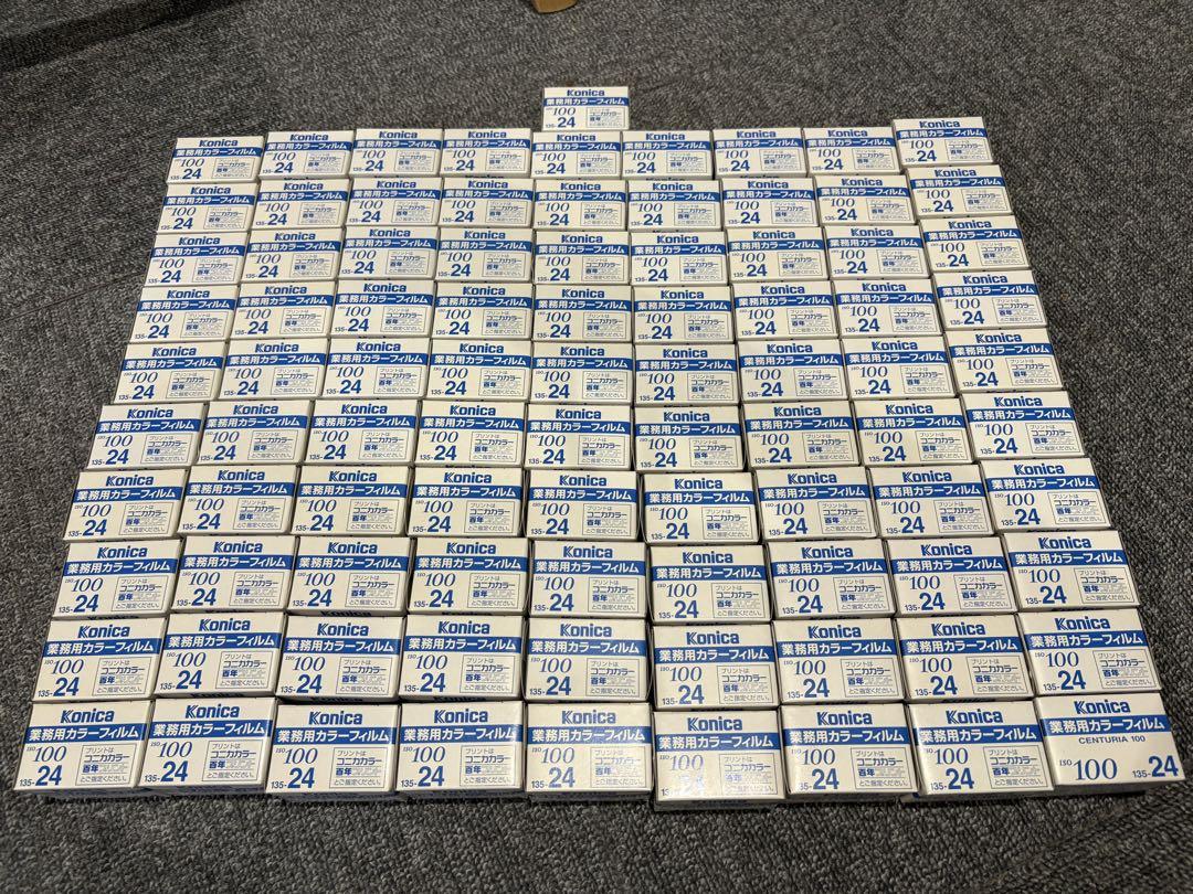 Many boxed Konica ISO100 24-exposure color film rolls arranged on a carpeted floor.