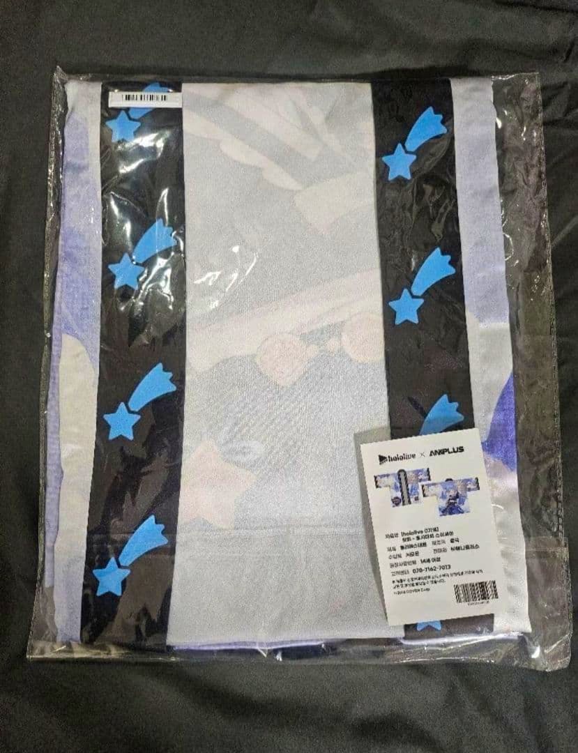 Folded polyester happi coat (法被) in clear plastic packaging showing black panels with blue shooting-star motifs and a product label.