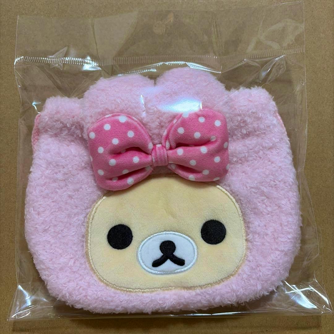 Front view of a pink Korilakkuma (rabbit) pop-up die-cut plush drawstring pouch with a pink polka-dot bow and embroidered face, in clear plastic packaging.