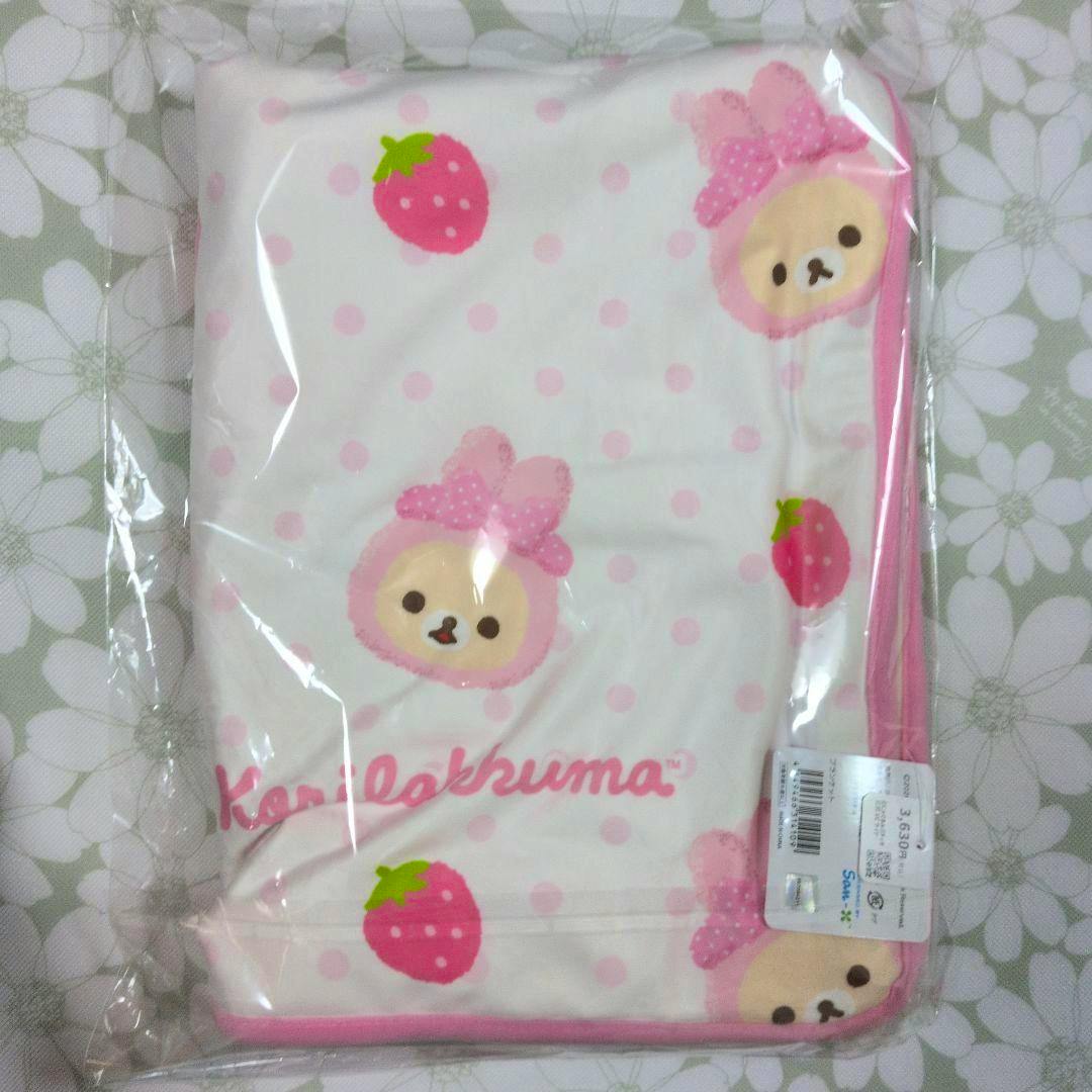 A folded Korilakkuma rabbit pop up blanket with pink polka dots, strawberries, and character faces in clear plastic packaging.