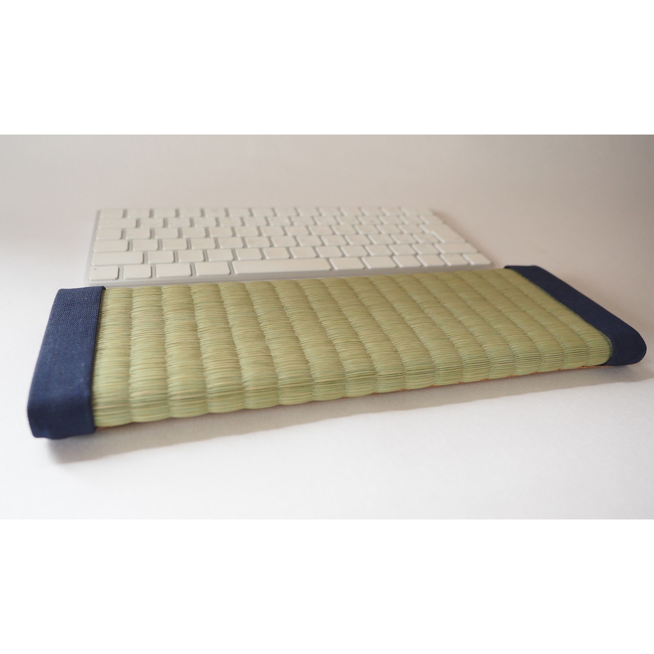 Tatami-style palm rest with woven rush surface and dark fabric end caps placed in front of a white keyboard.