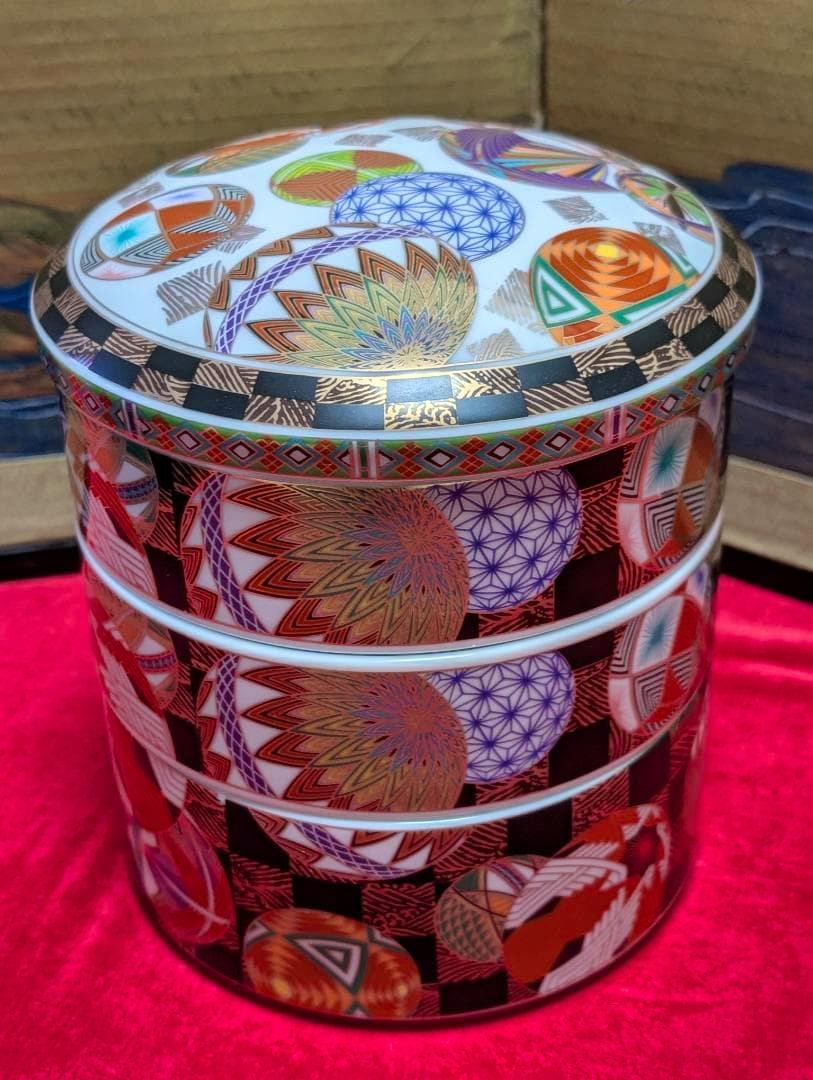 Colorful three-tiered temari-patterned stacking box with lid displayed on red cloth.