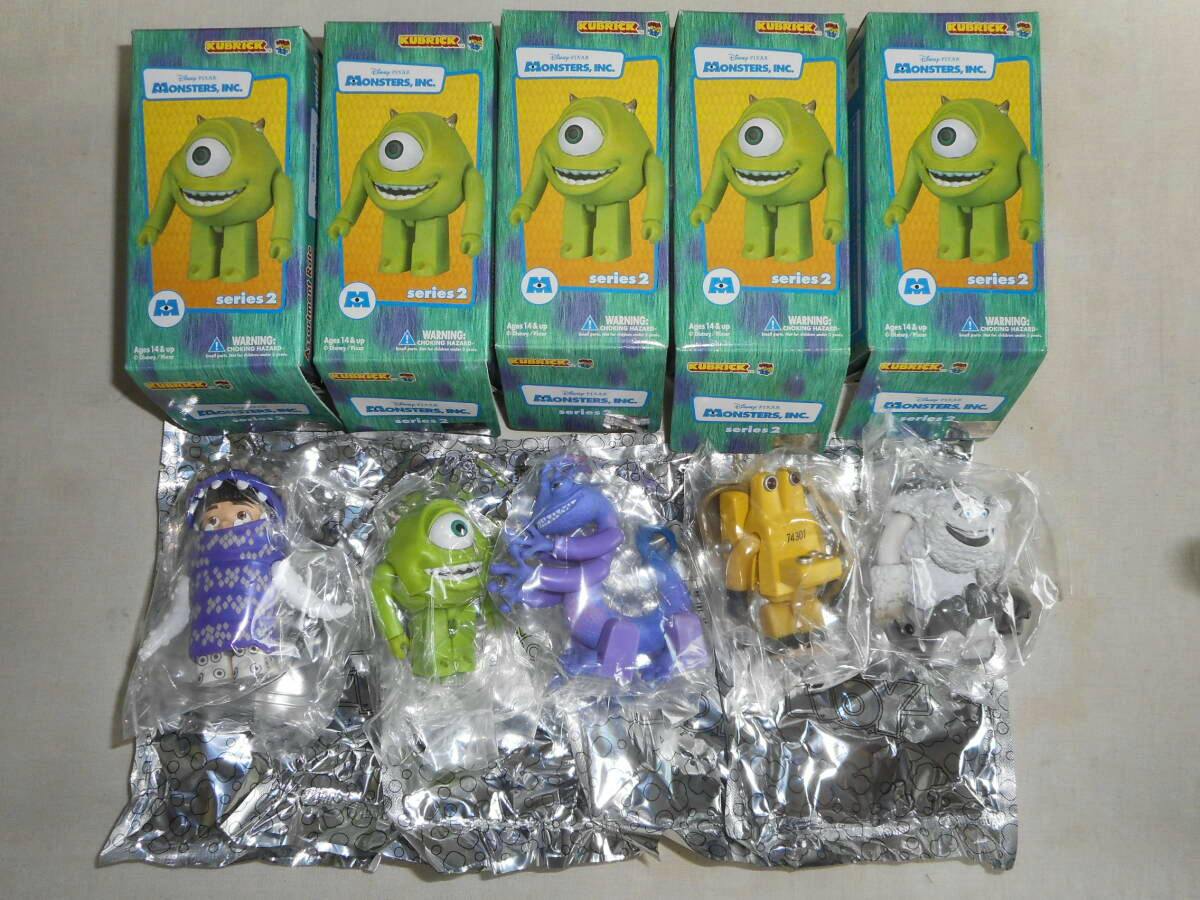 Five KUBRICK Monsters, Inc. Series 2 boxed figures arranged in a row above the five individual plastic figures sealed in clear bags.