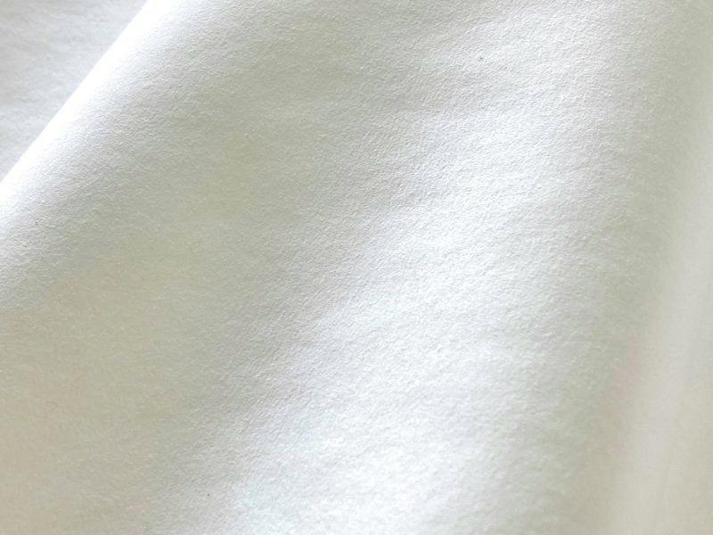 Close-up of white suede-like artificial leather fabric draped to show its texture.