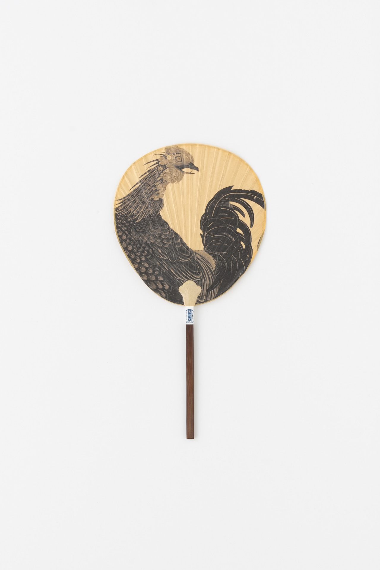Small round paper fan with a black rooster illustration on its face and a brown handle.