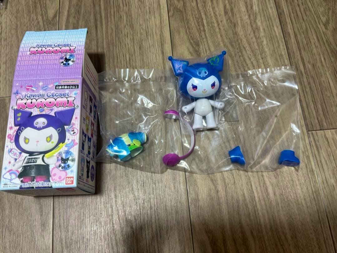 A disassembled Kuromi Kawaii Closet plastic figure and its product box laid out on a wooden floor.