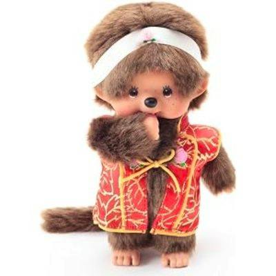 Front view of a Monchichi plush toy wearing a red and gold patterned jacket and a white headband.