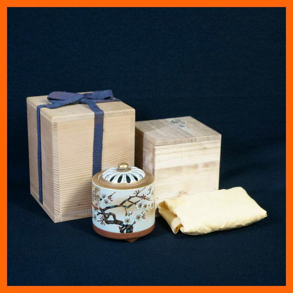 Ceramic incense burner with plum-branch decoration shown with two wooden storage boxes and a cloth on a dark background.