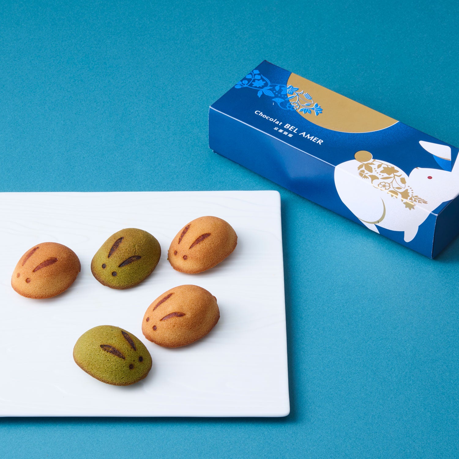 Five rabbit-shaped cakes on a white plate next to the product's blue packaging box.