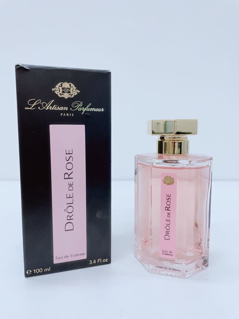 L'Artisan Parfumeur Drôle de Rose perfume bottle filled with pink liquid beside its black and pink box.