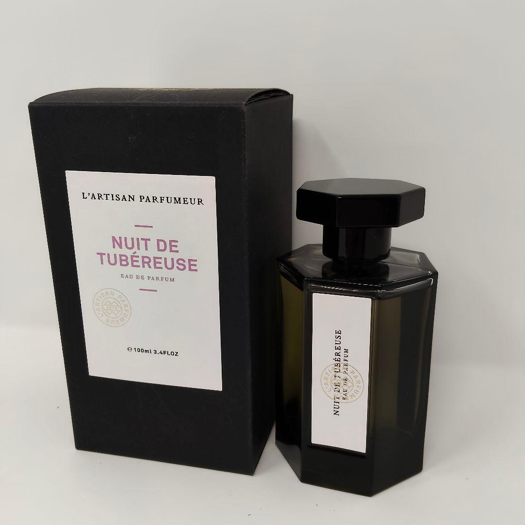 Bottle of L'Artisan Parfumeur Nuit de Tubéreuse perfume displayed next to its black box on a white background.