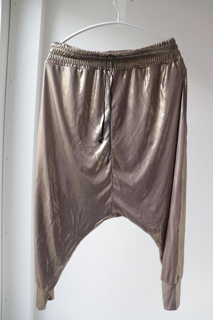 Front view of gold shiny men's sarouel-style polyester pants hanging on a hanger against a white background.